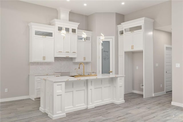 kitchen featuring an island with sink, white cabinets, decorative backsplash, and a sink