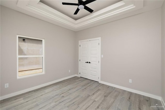 unfurnished room featuring a ceiling fan, a tray ceiling, baseboards, and wood finished floors