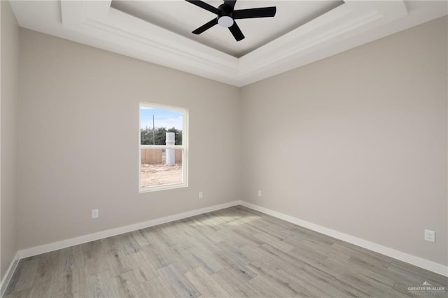 unfurnished room featuring light wood-style flooring, a tray ceiling, and baseboards