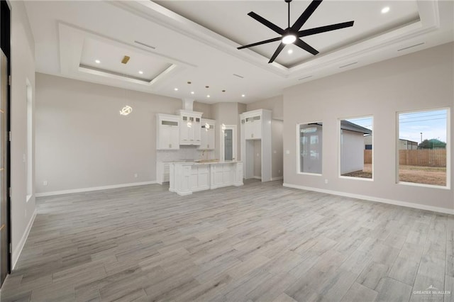 unfurnished living room featuring a ceiling fan, light wood-type flooring, a raised ceiling, and baseboards