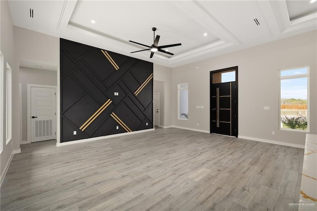 unfurnished living room featuring a tray ceiling, light wood finished floors, visible vents, ceiling fan, and baseboards