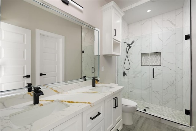 full bathroom featuring double vanity, a marble finish shower, a sink, and toilet