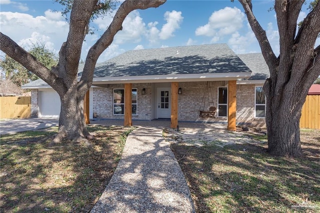 view of front of property with brick siding, an attached garage, a shingled roof, and fence