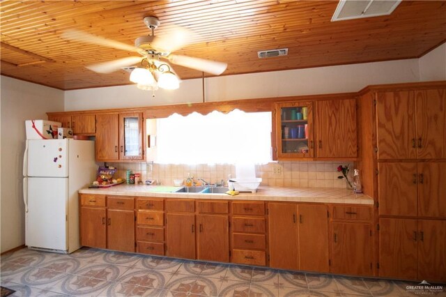 11009 Monte Cristo Rd, Edcouch, TX 78538 - kitchen with freestanding refrigerator, tile counters, wood ceiling, brown cabinets, and backsplash