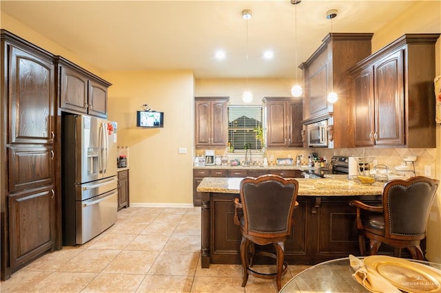 kitchen featuring dark brown cabinetry, light stone countertops, hanging light fixtures, and appliances with stainless steel finishes