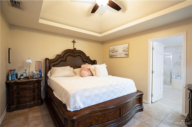 tiled bedroom with ensuite bathroom, ceiling fan, and a tray ceiling