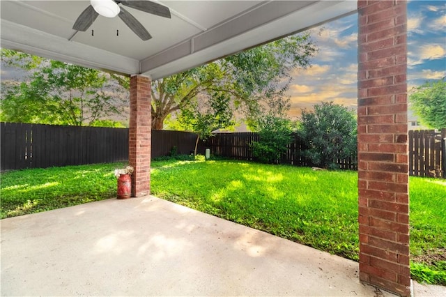 yard at dusk featuring ceiling fan and a patio area