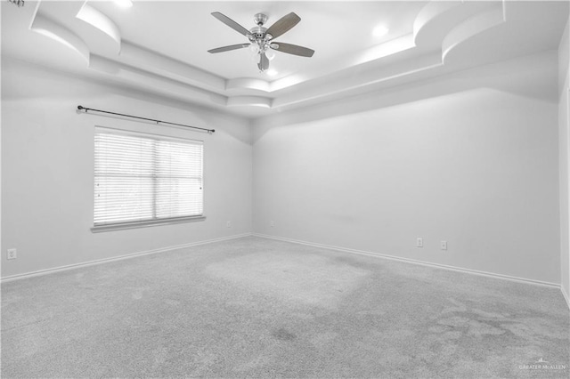 empty room featuring carpet, a tray ceiling, and ceiling fan