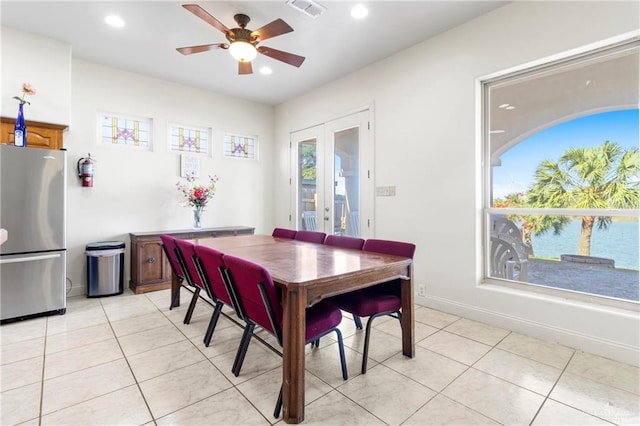 tiled dining room with ceiling fan, french doors, a healthy amount of sunlight, and a water view