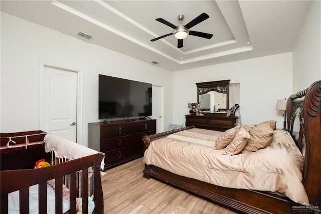 bedroom with ceiling fan, a tray ceiling, and light hardwood / wood-style flooring