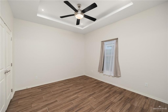 spare room with ceiling fan, a raised ceiling, and dark wood-type flooring