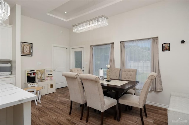 dining area with a raised ceiling, dark hardwood / wood-style flooring, a towering ceiling, and a chandelier