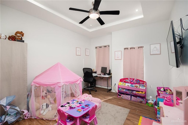 recreation room with a tray ceiling, ceiling fan, and wood-type flooring