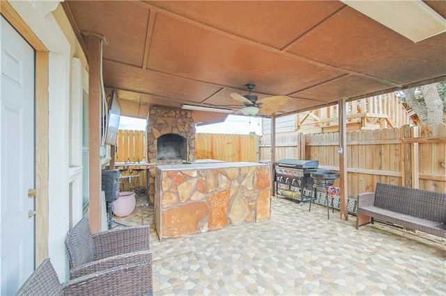 view of patio / terrace featuring ceiling fan, exterior bar, a stone fireplace, and a grill