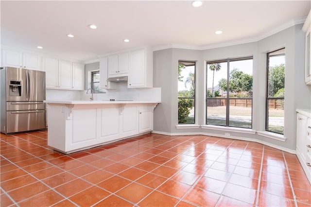 kitchen featuring a kitchen bar, stainless steel fridge, kitchen peninsula, white cabinets, and plenty of natural light