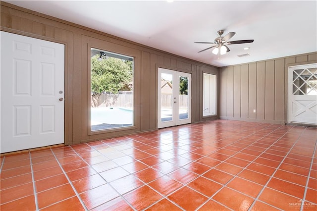 doorway with tile patterned floors, ceiling fan, and wood walls