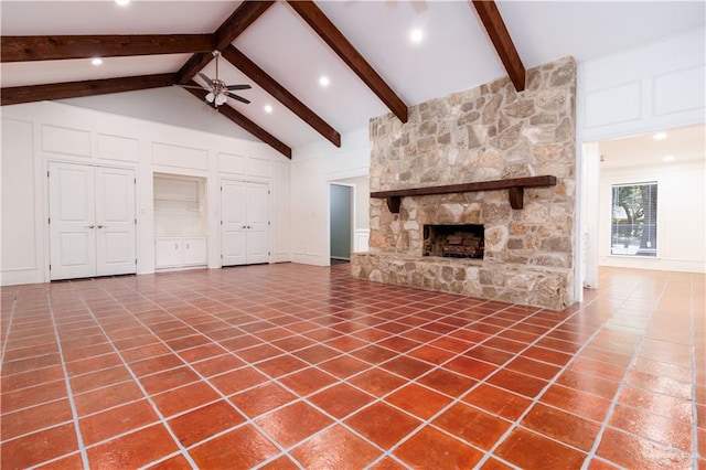 unfurnished living room featuring high vaulted ceiling, tile patterned floors, a stone fireplace, ceiling fan, and beamed ceiling