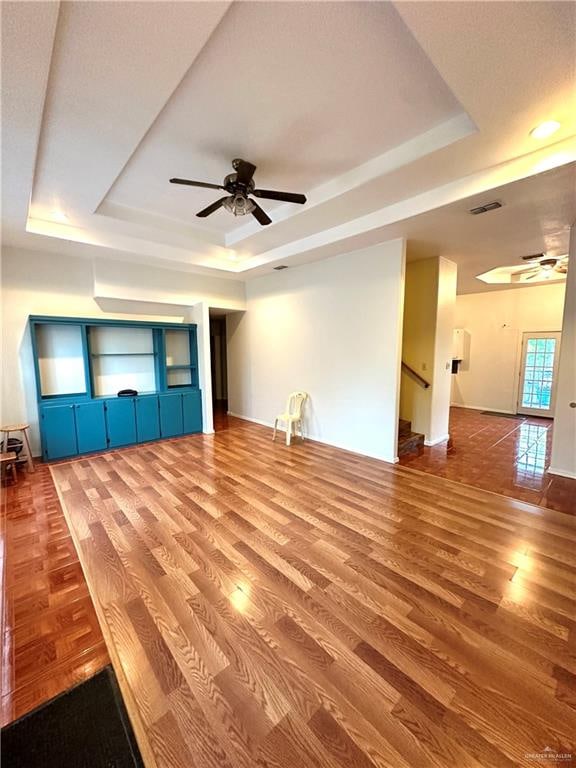 unfurnished living room featuring a raised ceiling, ceiling fan, and hardwood / wood-style flooring