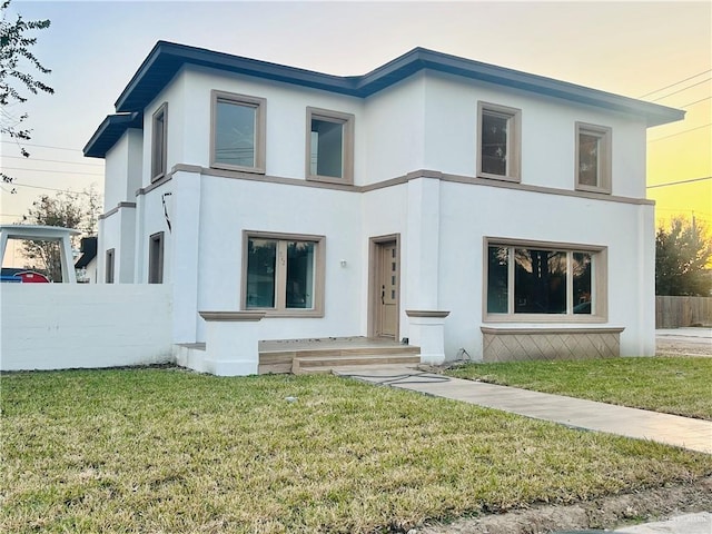 view of front of house featuring fence, a front lawn, and stucco siding