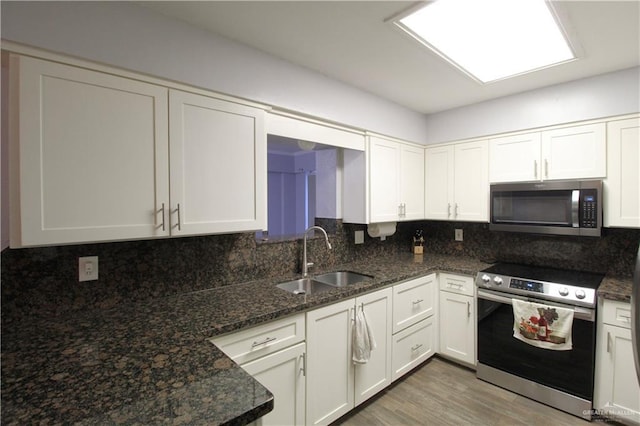 kitchen with dark stone countertops, a sink, white cabinets, appliances with stainless steel finishes, and backsplash