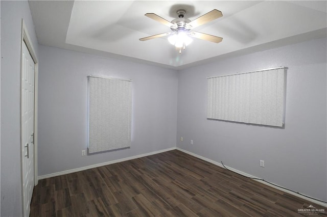 spare room with a tray ceiling, baseboards, wood finished floors, and a ceiling fan