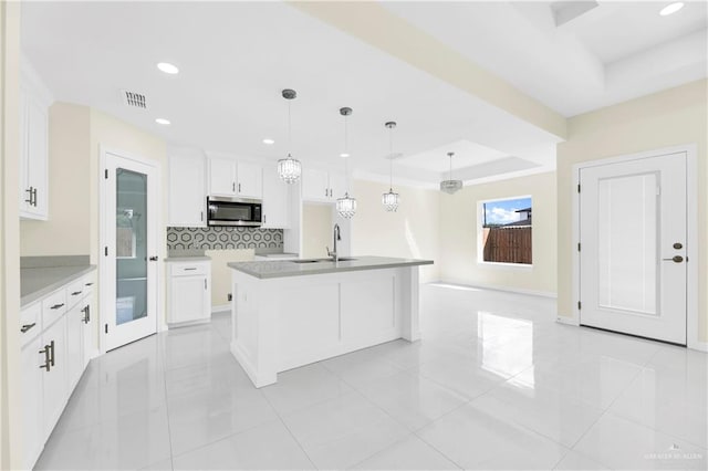 kitchen with decorative light fixtures, white cabinetry, a tray ceiling, and an island with sink