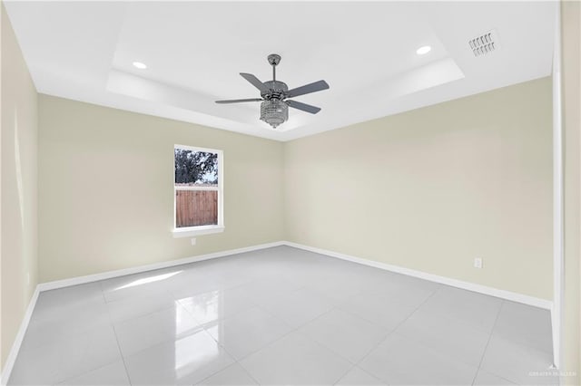 tiled empty room with a raised ceiling and ceiling fan