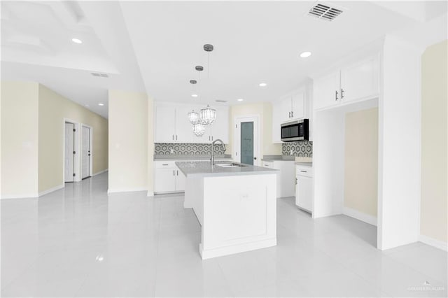 kitchen with backsplash, sink, a center island with sink, white cabinetry, and hanging light fixtures