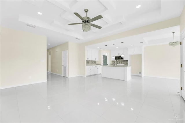 unfurnished living room with coffered ceiling, a raised ceiling, ceiling fan, sink, and light tile patterned floors