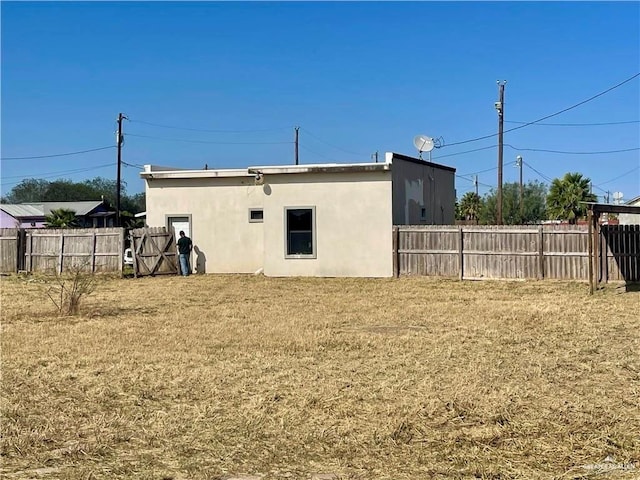 rear view of property featuring a yard, fence, and stucco siding