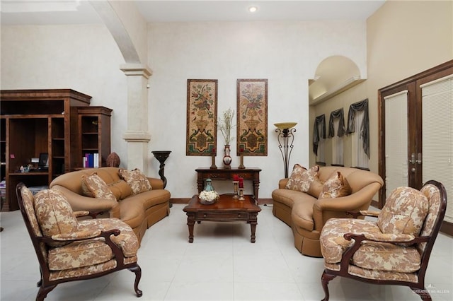 tiled living area featuring baseboards, arched walkways, and ornate columns