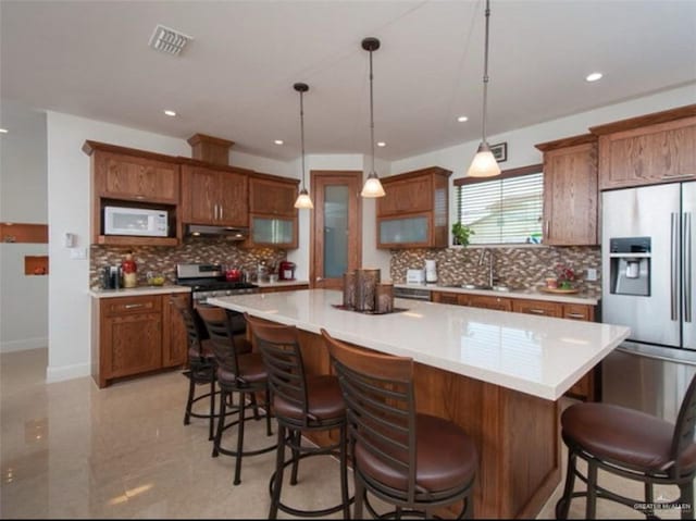 kitchen with appliances with stainless steel finishes, a kitchen breakfast bar, a spacious island, sink, and hanging light fixtures