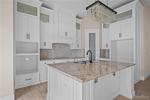 kitchen featuring backsplash, light stone counters, white cabinetry, and an island with sink