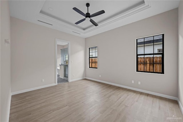 unfurnished room featuring ceiling fan, light wood-type flooring, and a tray ceiling