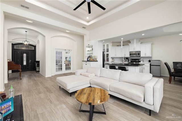 living room featuring french doors, a tray ceiling, ceiling fan with notable chandelier, and light hardwood / wood-style floors