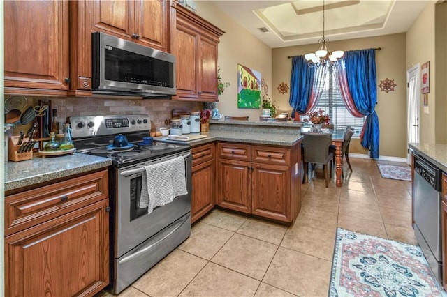 kitchen with kitchen peninsula, stainless steel appliances, a tray ceiling, light tile patterned floors, and an inviting chandelier