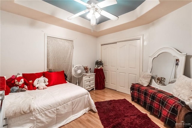 bedroom with a tray ceiling, light hardwood / wood-style flooring, a closet, and ceiling fan