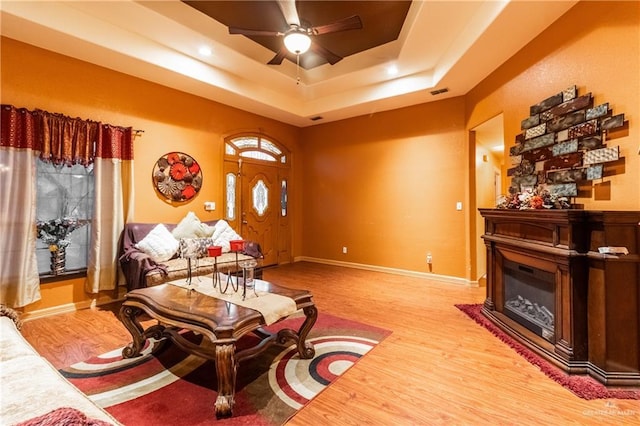 living room featuring a tray ceiling, light hardwood / wood-style flooring, and ceiling fan