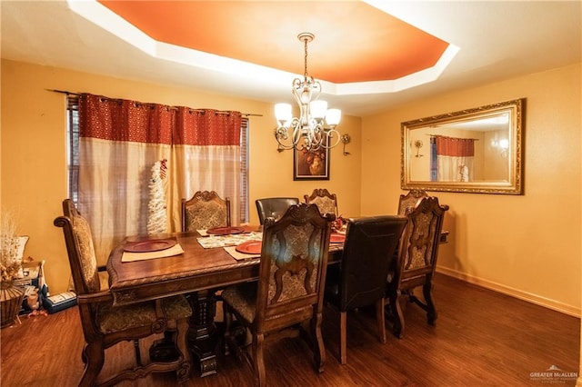 dining space with an inviting chandelier, hardwood / wood-style floors, and a raised ceiling