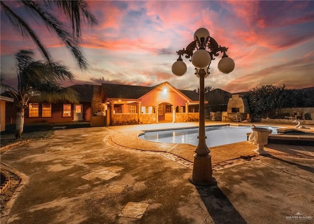 pool at dusk featuring a fireplace and a patio