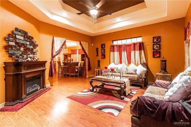 living room with light hardwood / wood-style flooring, a raised ceiling, and ceiling fan