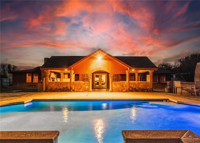 pool at dusk featuring a patio and an outbuilding