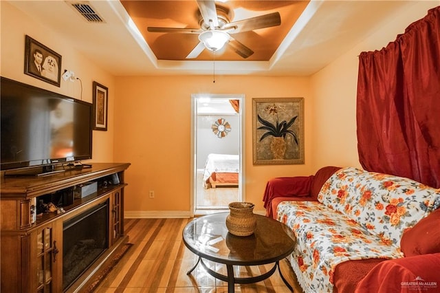 living room featuring a raised ceiling, light wood-type flooring, and ceiling fan