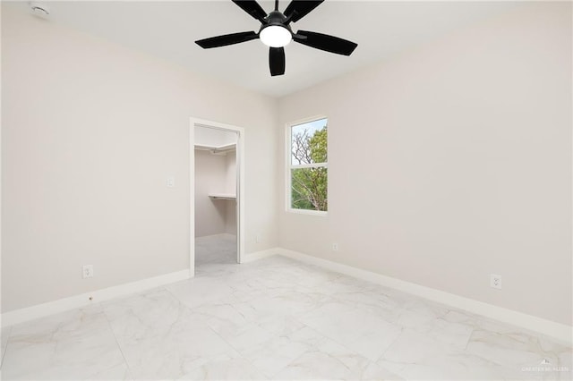 unfurnished bedroom featuring baseboards, marble finish floor, a walk in closet, and ceiling fan