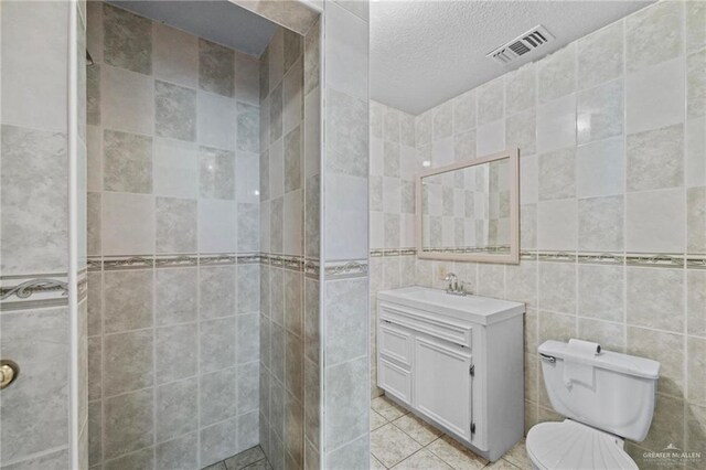 bathroom featuring tile patterned floors, a textured ceiling, vanity, tile walls, and toilet