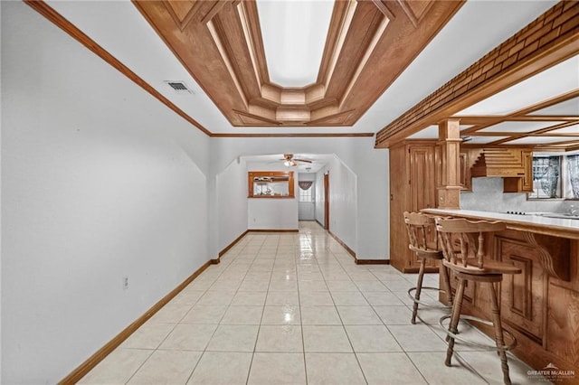 interior space with a kitchen breakfast bar, a raised ceiling, ceiling fan, ornamental molding, and light tile patterned flooring