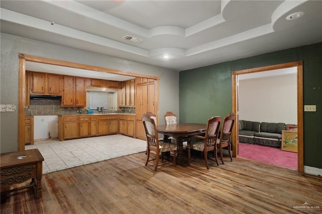 dining space with light wood-type flooring and a tray ceiling