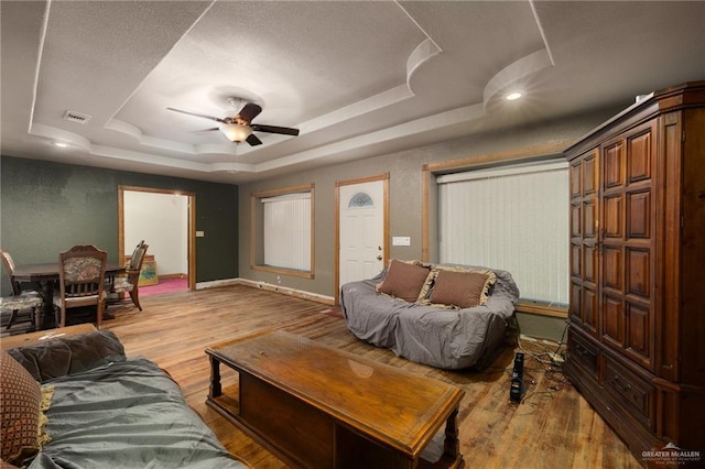 living room featuring a raised ceiling, ceiling fan, and light hardwood / wood-style flooring