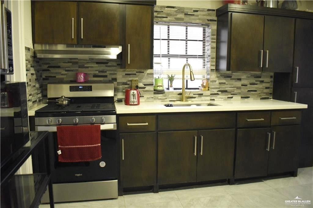 kitchen featuring light countertops, a sink, under cabinet range hood, and gas range