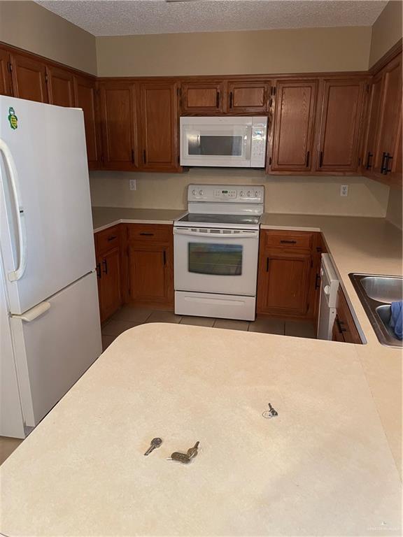 kitchen with white appliances, sink, a textured ceiling, light tile patterned flooring, and kitchen peninsula